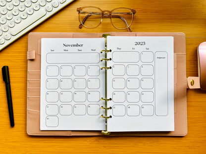 Open planner showing November 2025 calendar on a wooden desk with glasses and a keyboard.