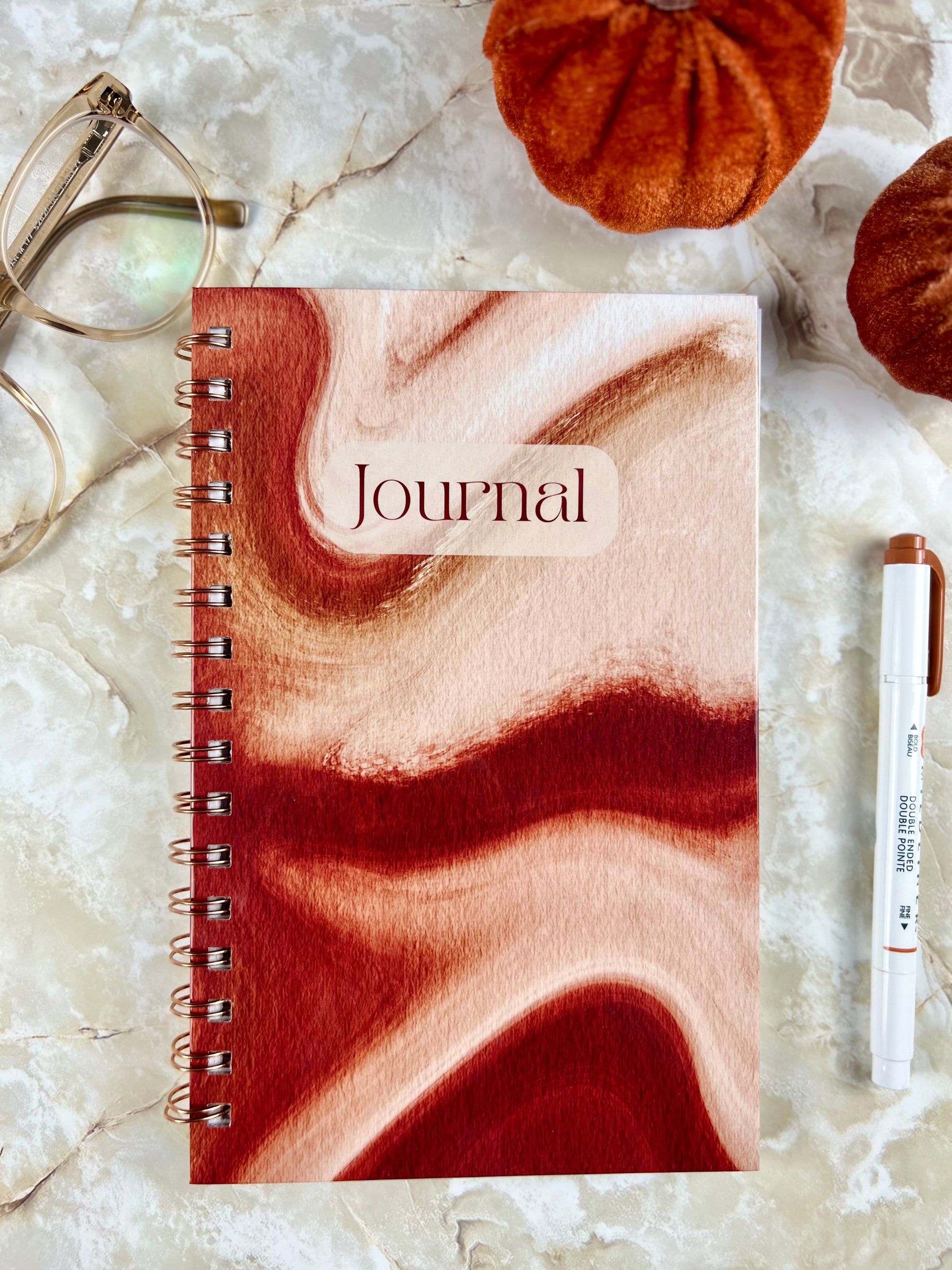 Journal with marbled design on a marble surface with a pen and small pumpkins.