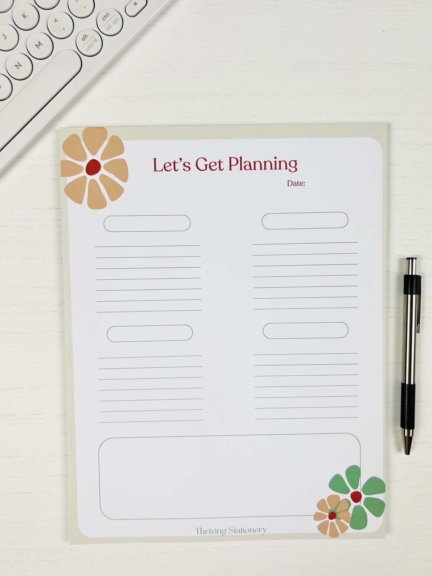 Planning notepad with floral designs and text on a white surface with a pen and keyboard.