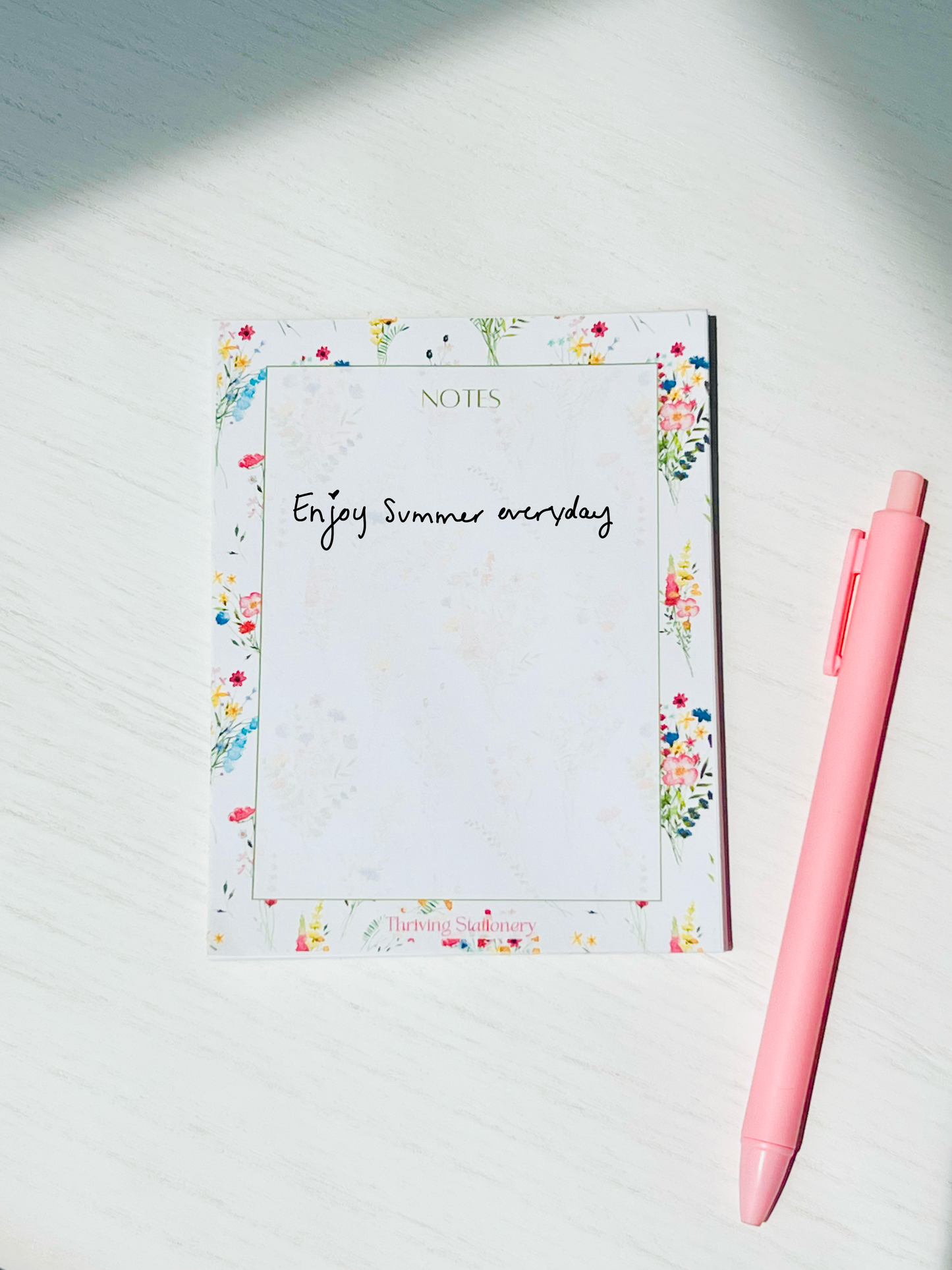White notepad bordered with vibrant watercolor wildflowers. The word “NOTES” is printed at the top in a soft green serif font. Branding at the bottom reads “Thriving Stationery.”
