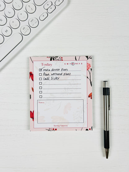 Pink Botanical Daily Planner Notepad with floral border, to-do list, and notes section with a pen and keyboard for scale