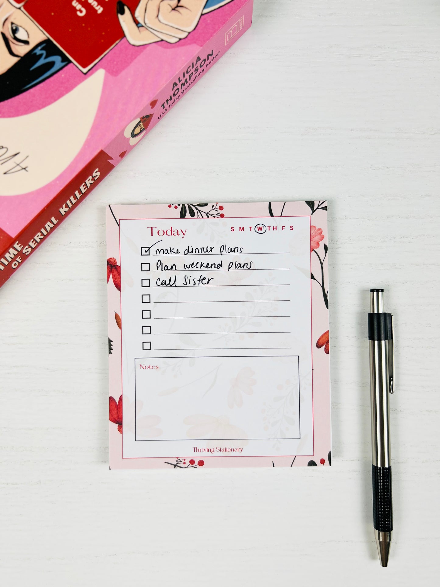 Pink Botanical Daily Planner Notepad with floral border, to-do list, and notes section with a pen for scale