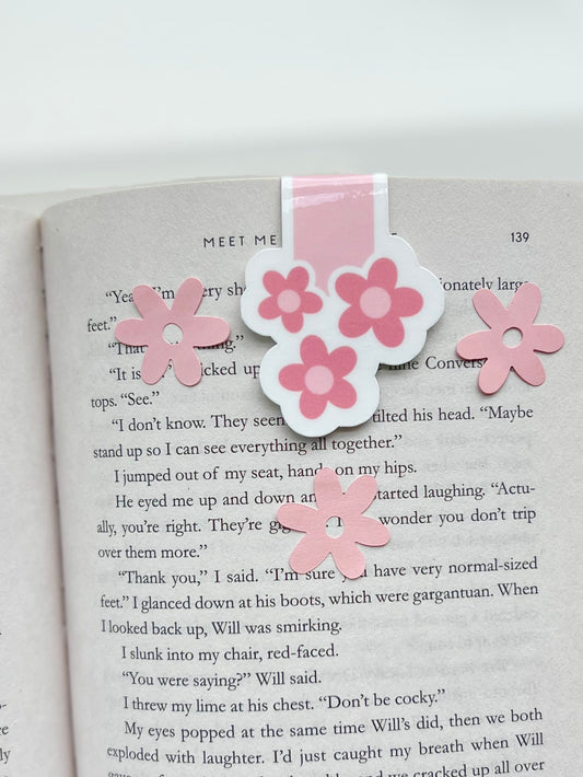 A magnetic bookmark with a pink floral design attached to an open book.