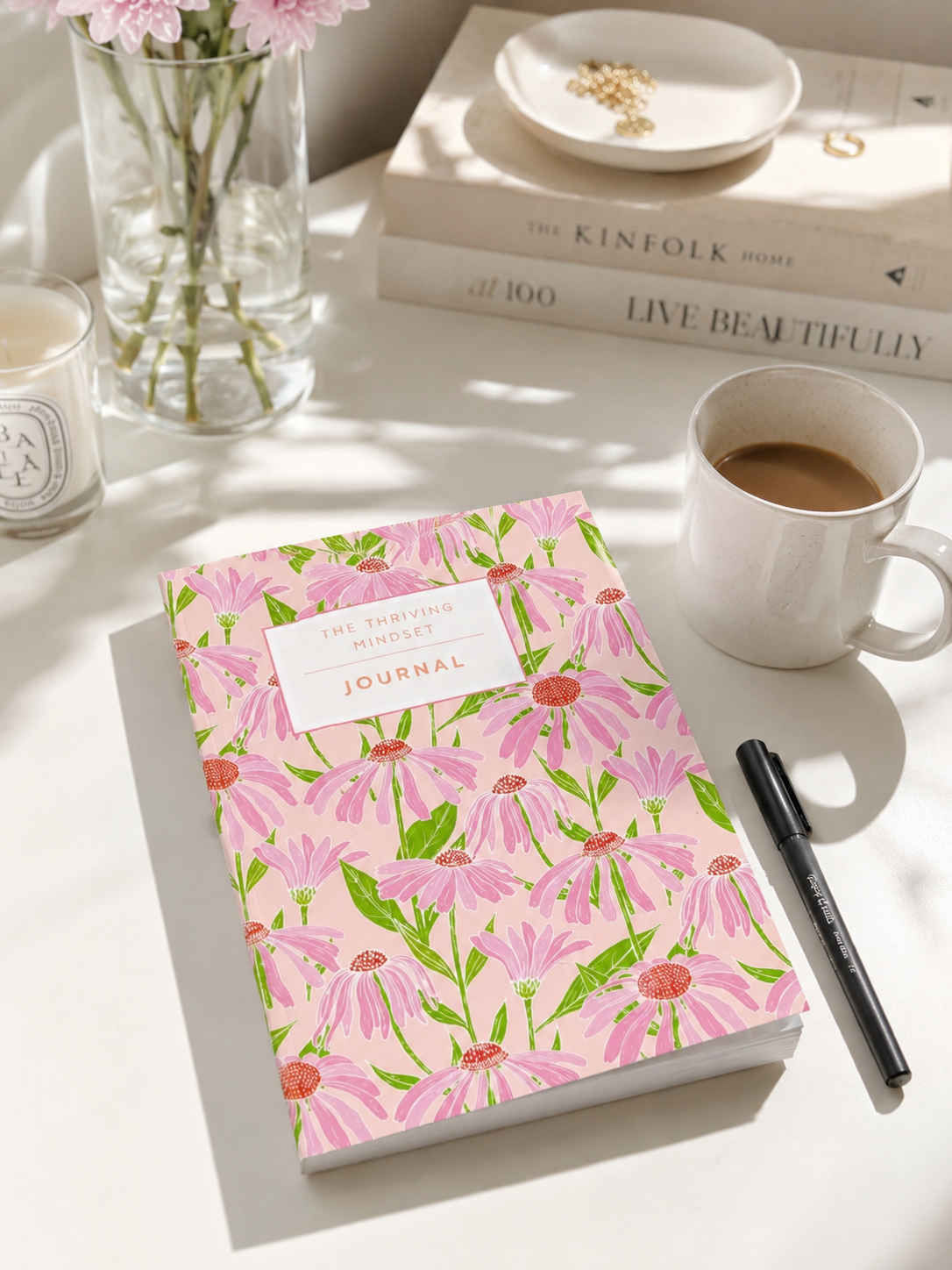 Floral journal on a table with a cup of coffee, books, and a candle.
