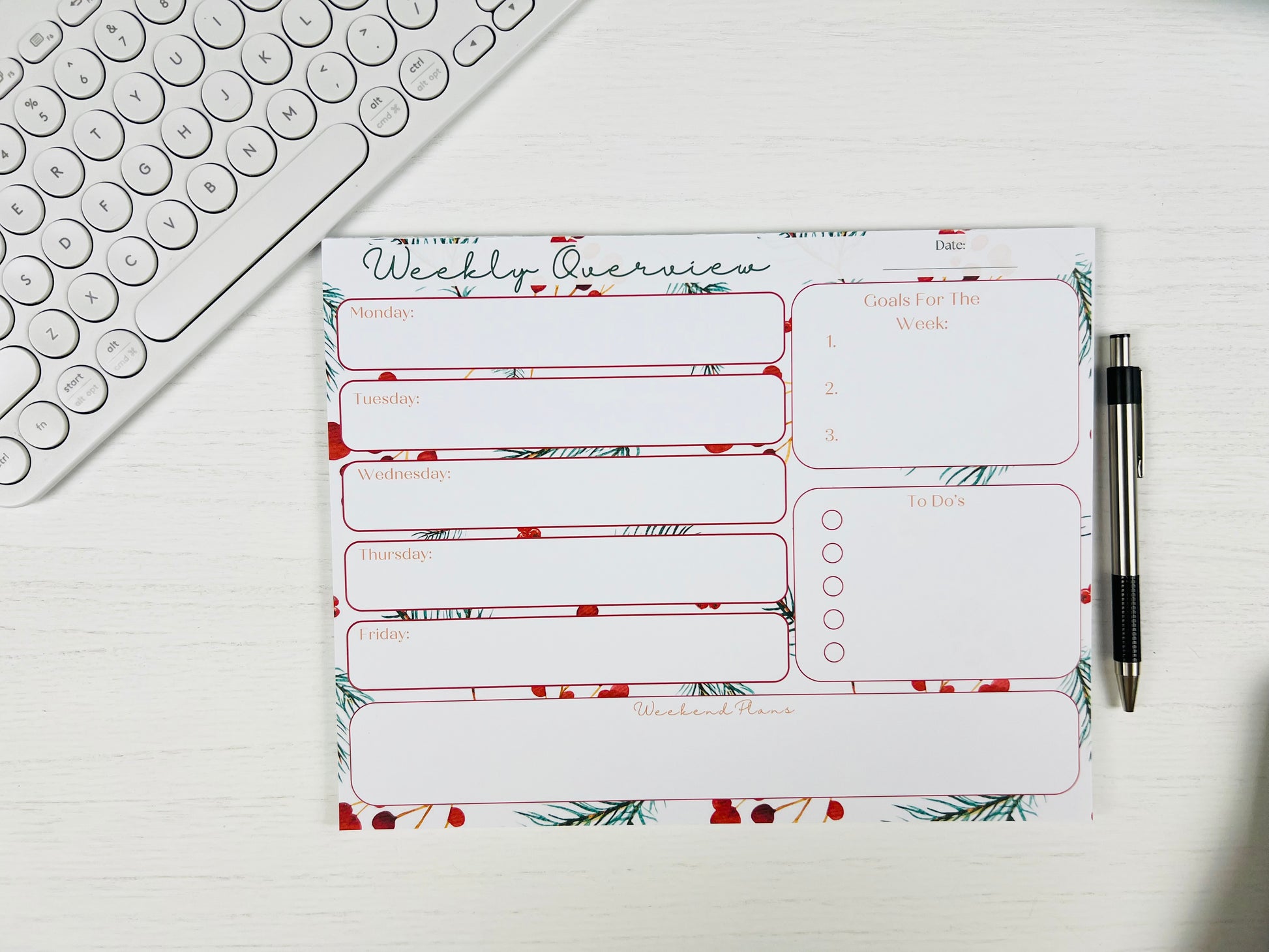 Weekly planner pad with floral design on a desk with a keyboard and pen.