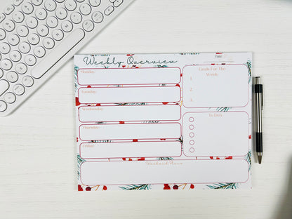 Weekly planner pad with floral design on a desk with a keyboard and pen.