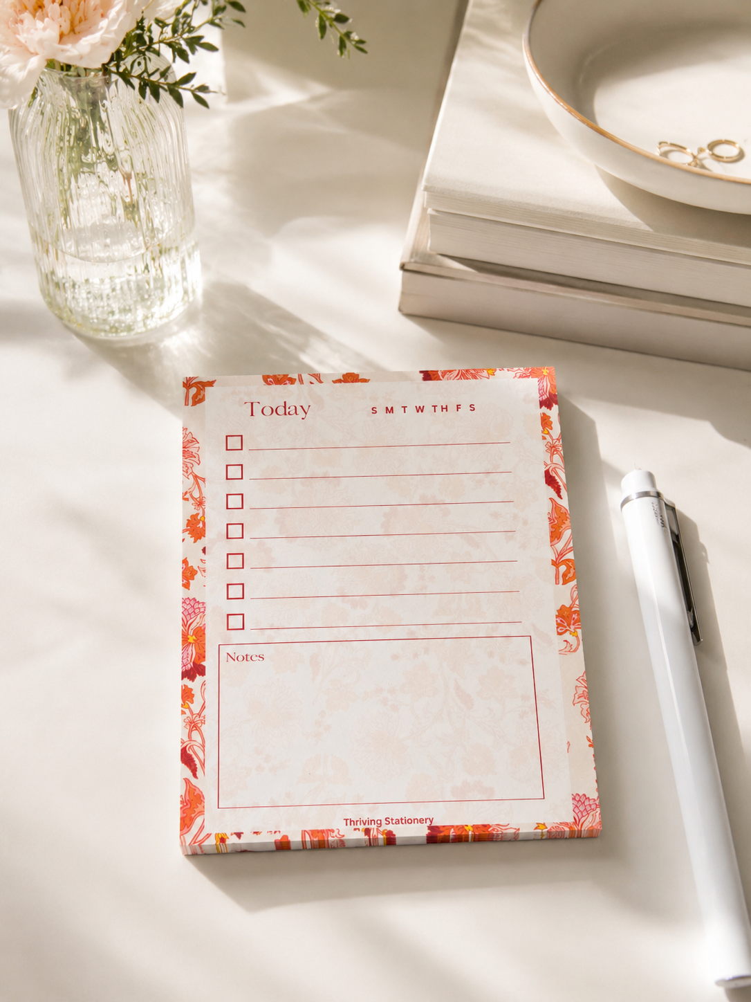 Notepad with floral design on a light surface with a pen and decorative items.