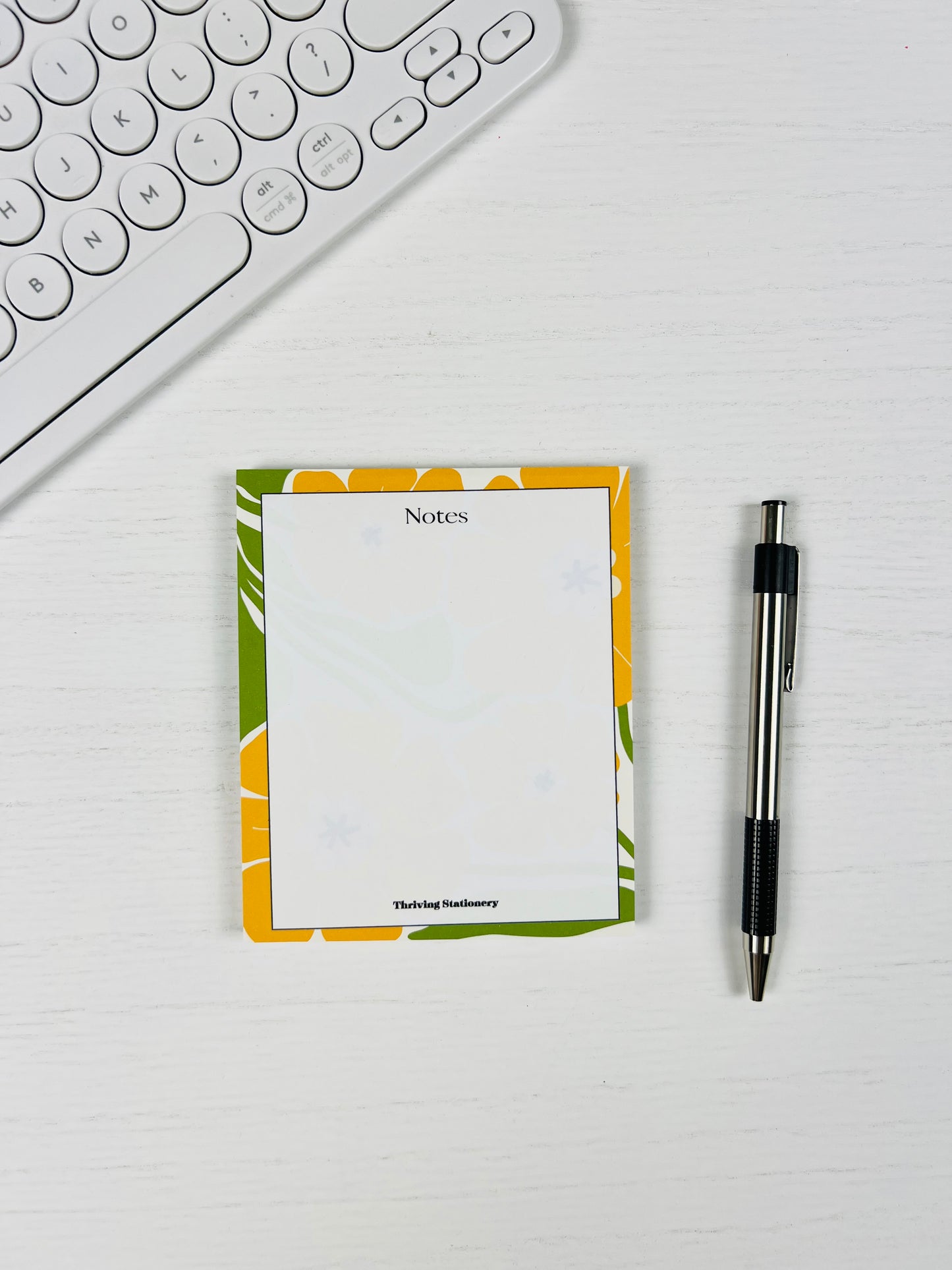 Notepad with floral design and pen on a white surface next to a keyboard