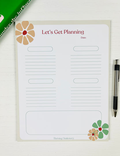 Planning pad with floral designs and text on a white surface with a pen.