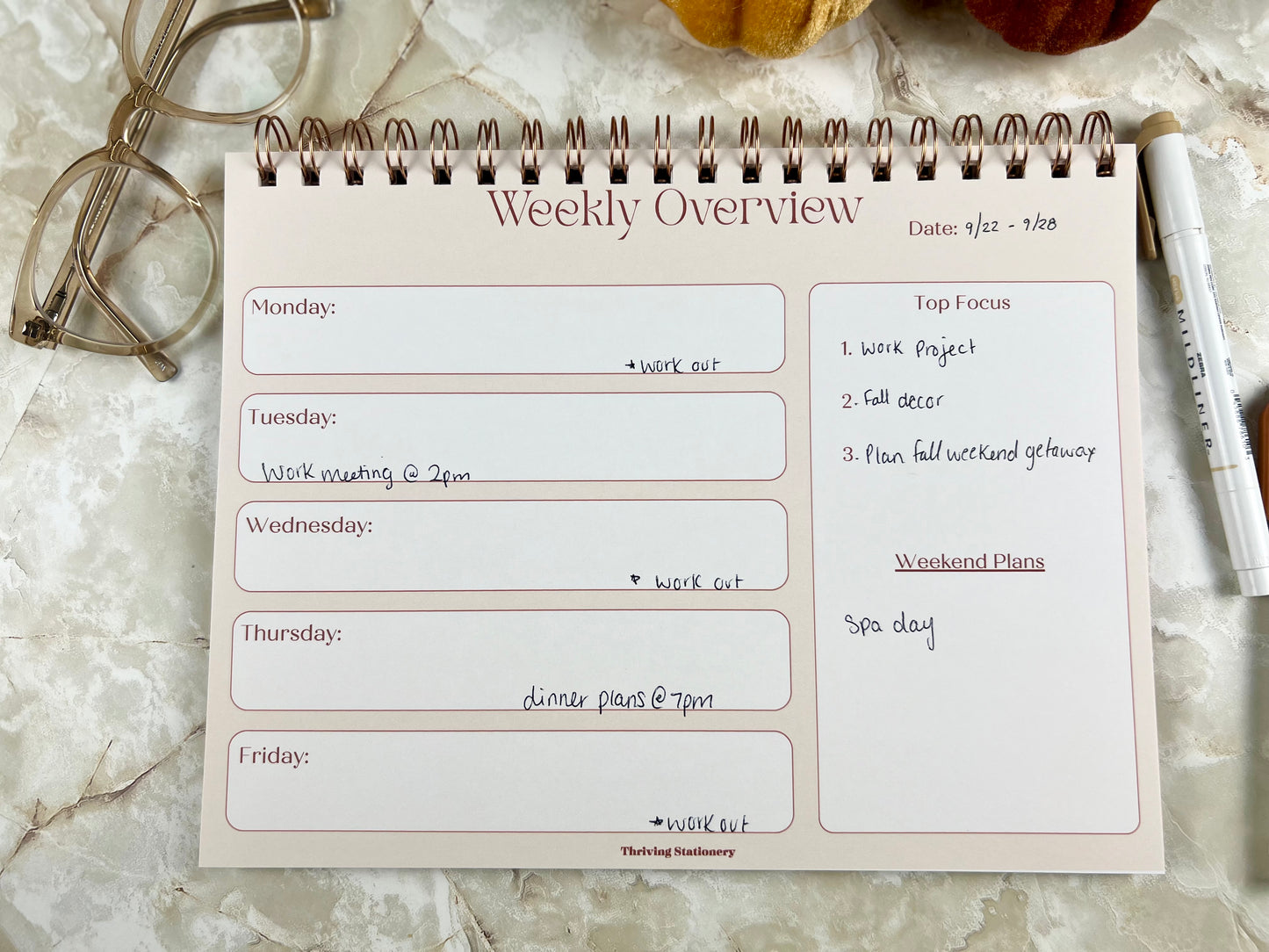 Weekly overview planner on a marble surface with glasses and pen.