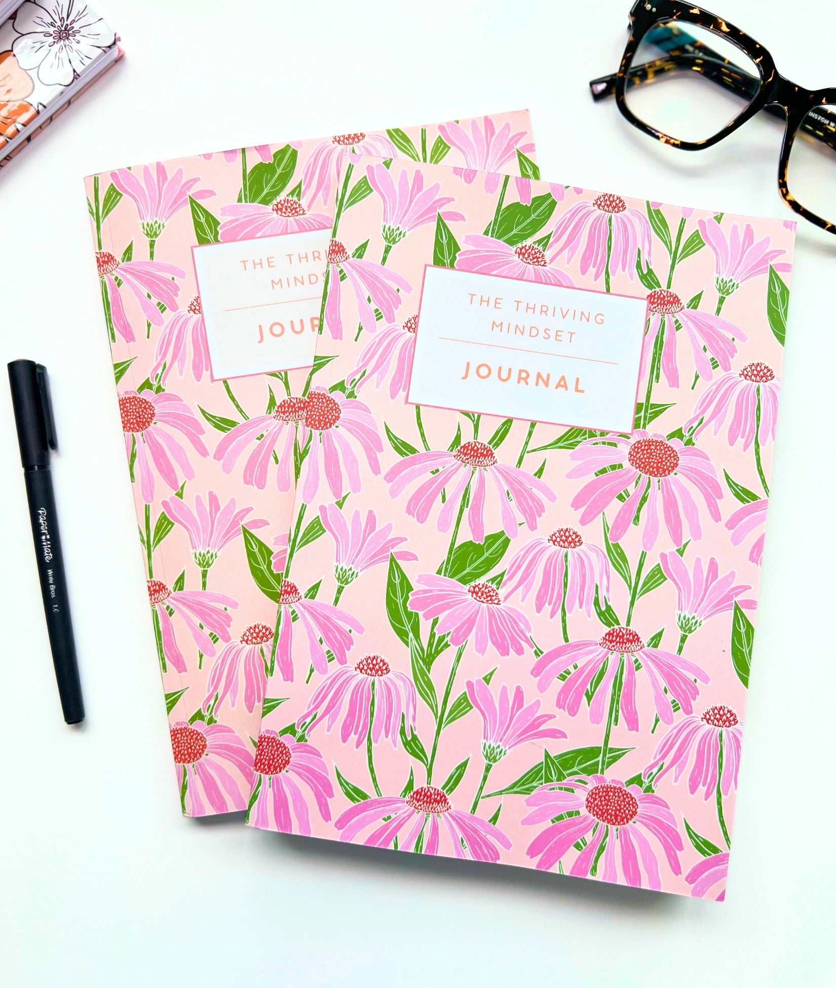 Floral patterned journals on a white surface with a pen and glasses.
