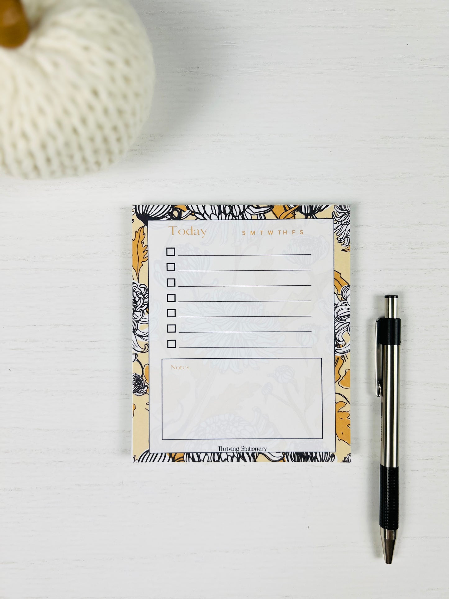 Floral-themed notepad with a pen on a white surface