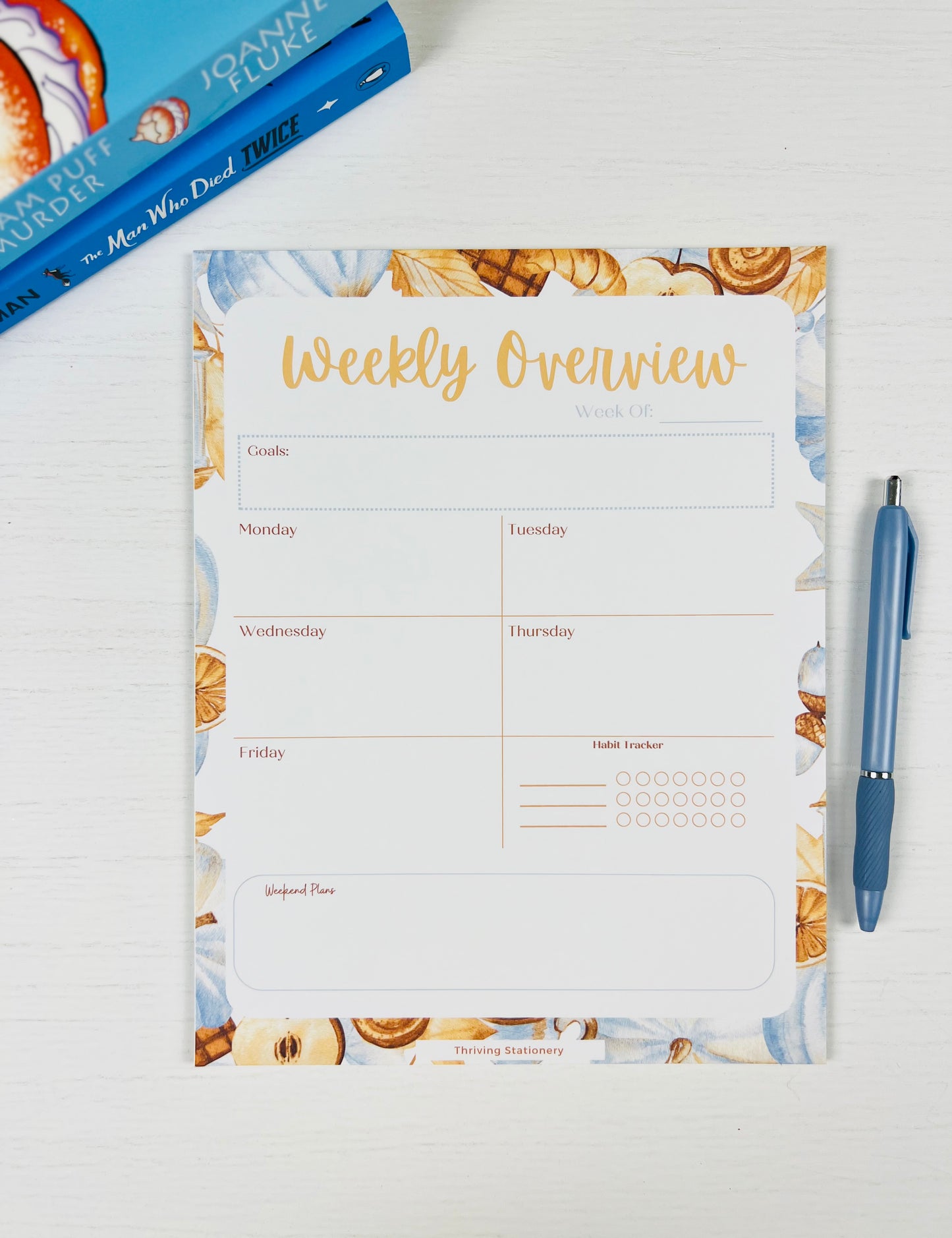 Warm & Cozy Weekly Planner Notepad with neutral cozy design and weekly layout with a book and pen for scale