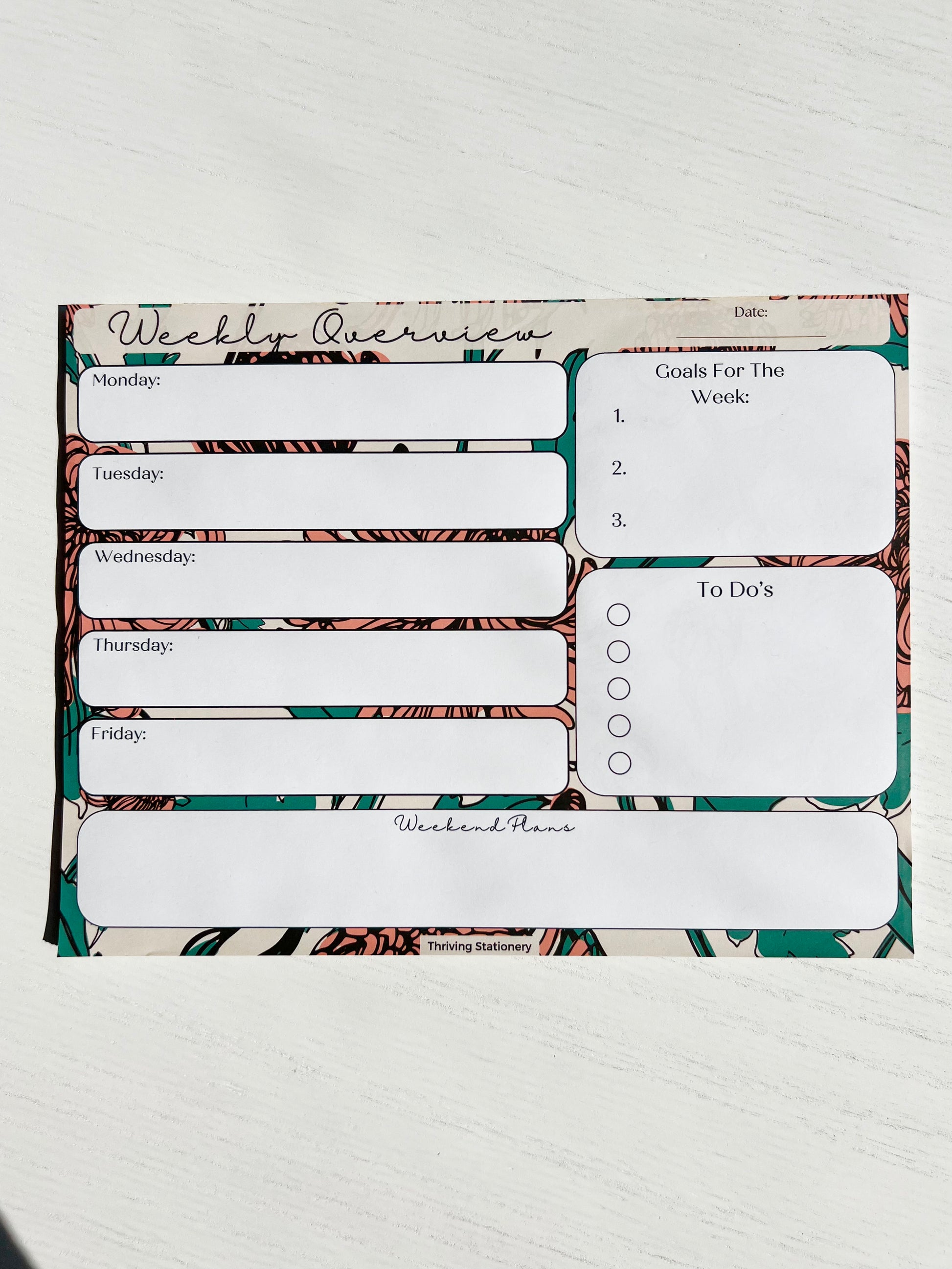 Weekly planner notepad with bold floral background featuring daily sections, weekly goals, to-do list with checkboxes, and weekend planning space.