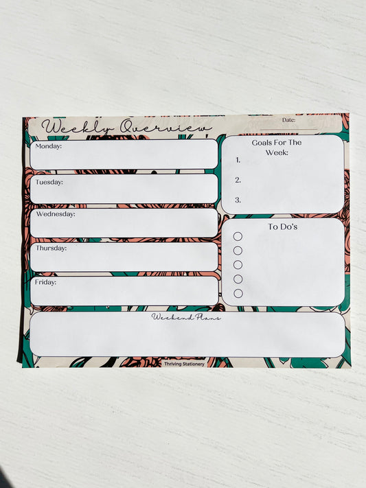 Weekly planner notepad with bold floral background featuring daily sections, weekly goals, to-do list with checkboxes, and weekend planning space.